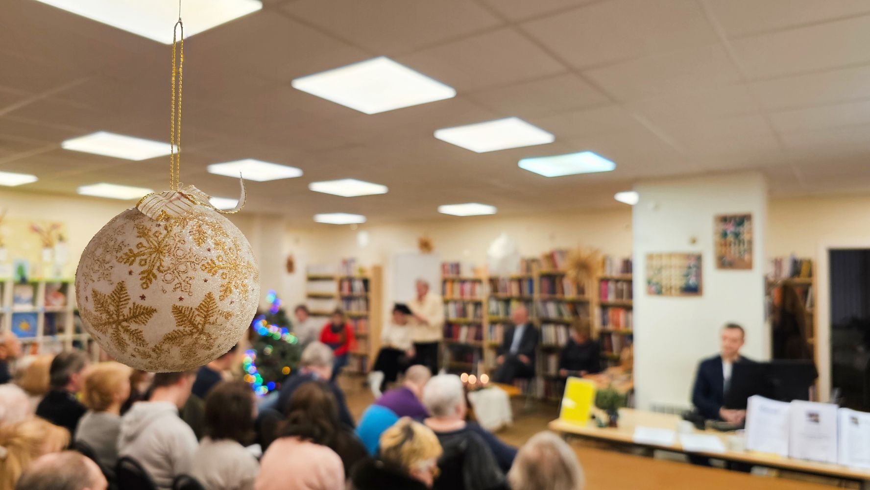 Tuvplānā Ziemassvētku rotājums. Fonā pasākuma apmeklētāji